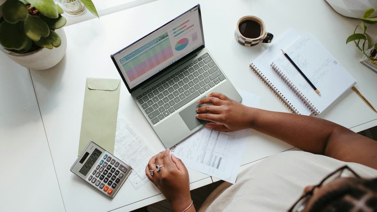 Overhead view of a laptop with charts, a calculator, and invoices on a desk, showing the real cost of getting one therapy client in Ontario